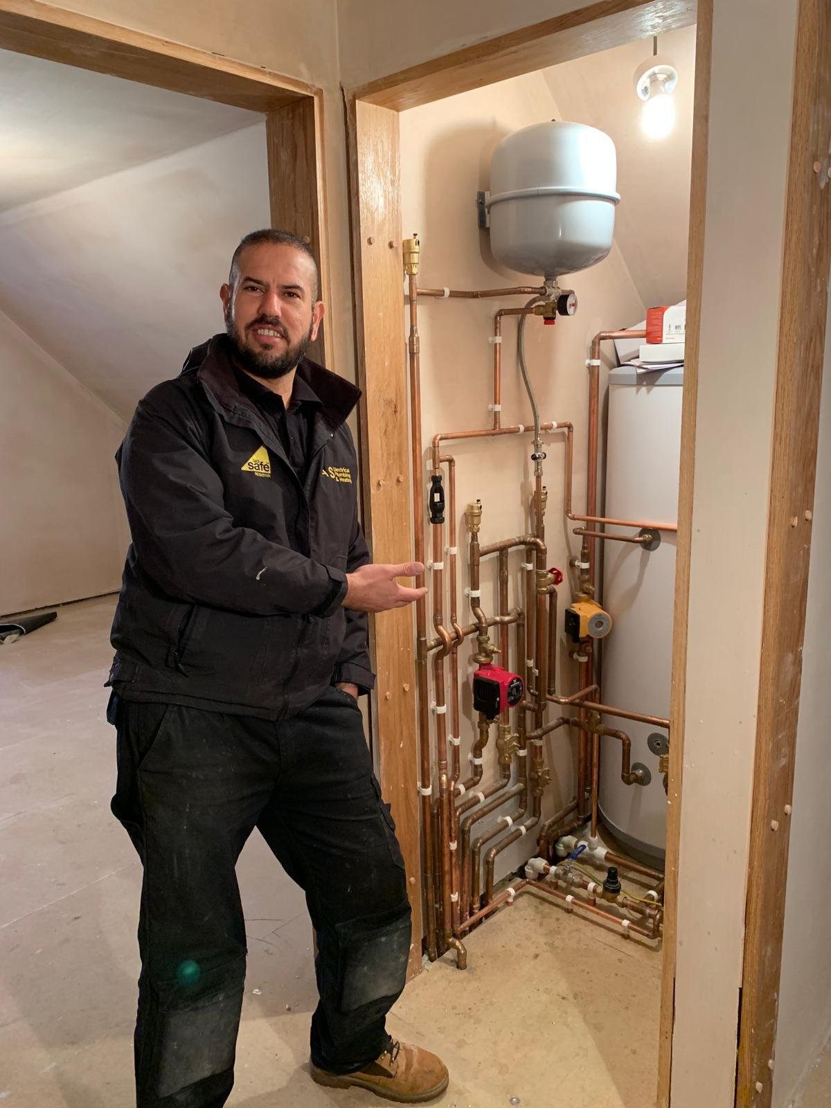 Gas Safe registered engineer beside a completed copper manifold and hot water cylinder