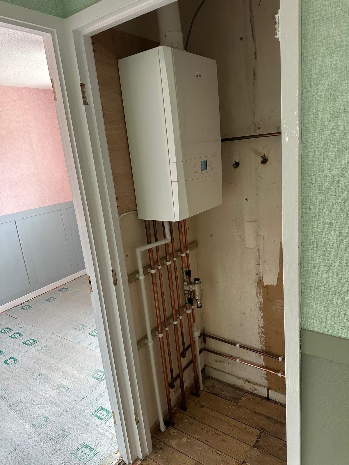 Ideal boiler and exposed copper risers in a cupboard during a heating system replacement