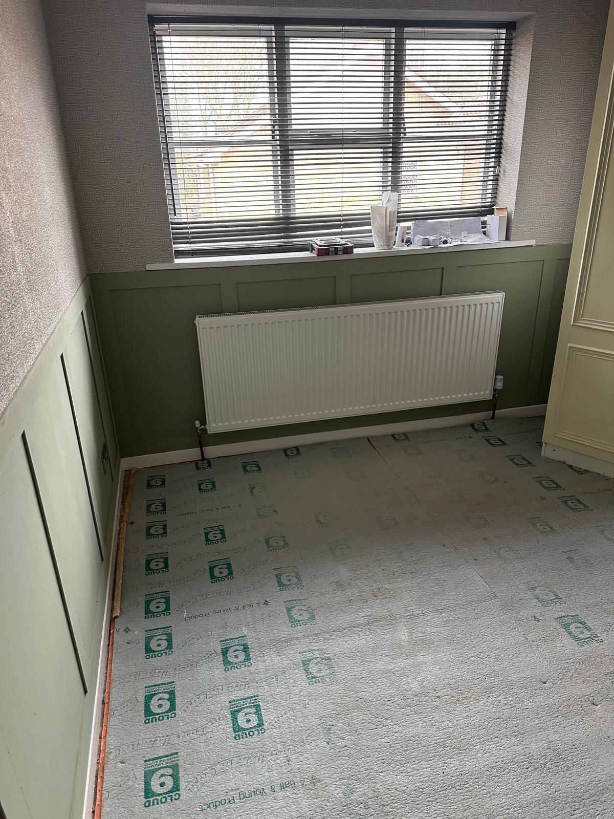 White double panel radiator installed beneath a window on a panelled wall with floor protection down