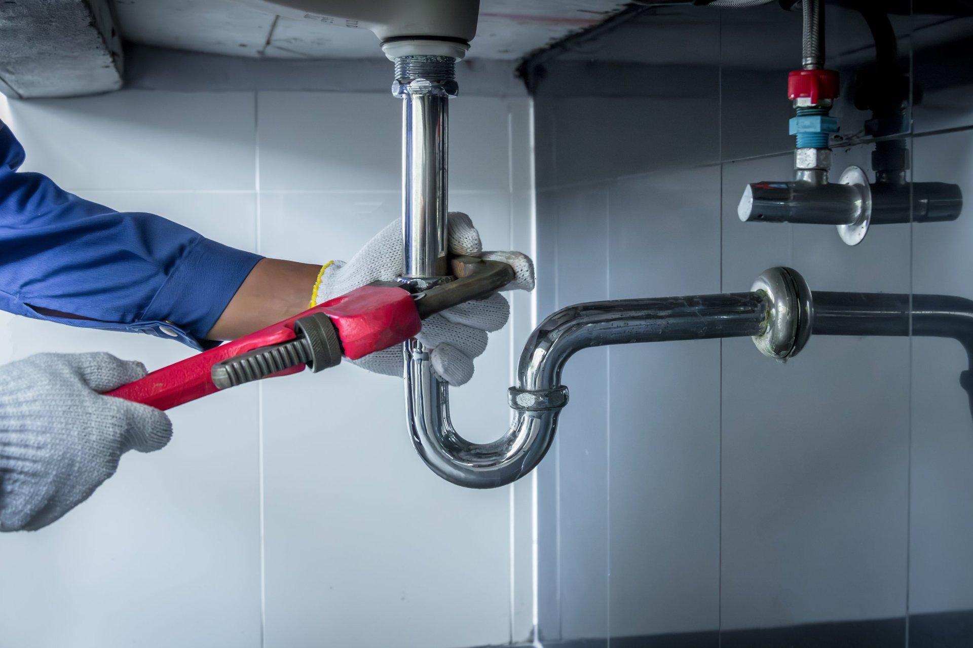 Plumber hands holding wrench repairing sink pipe in bathroom