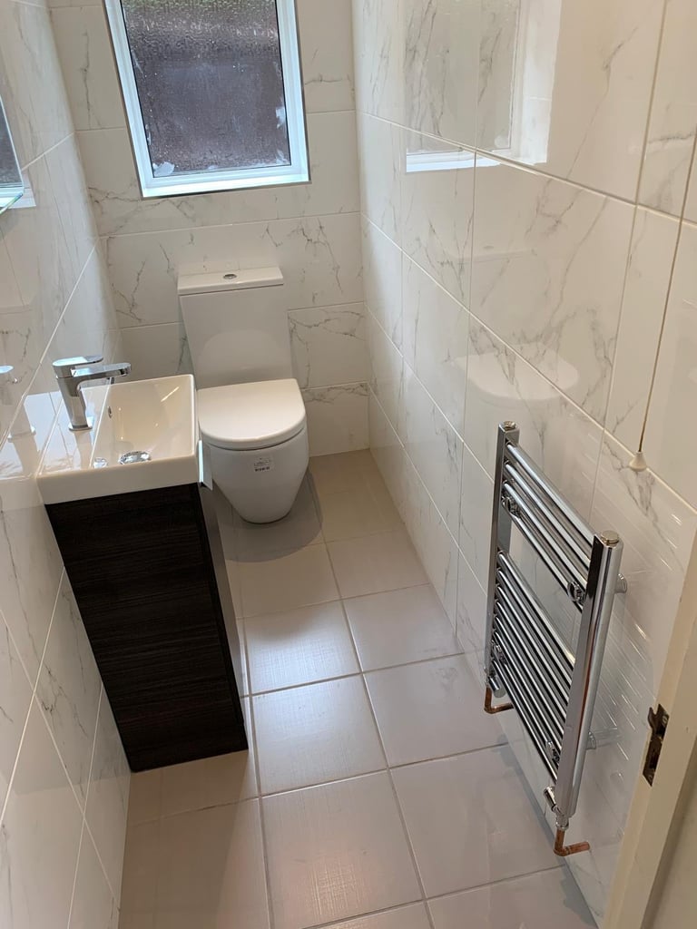 Modern bathroom with white tiled walls, toilet, sink vanity, towel rack, and window