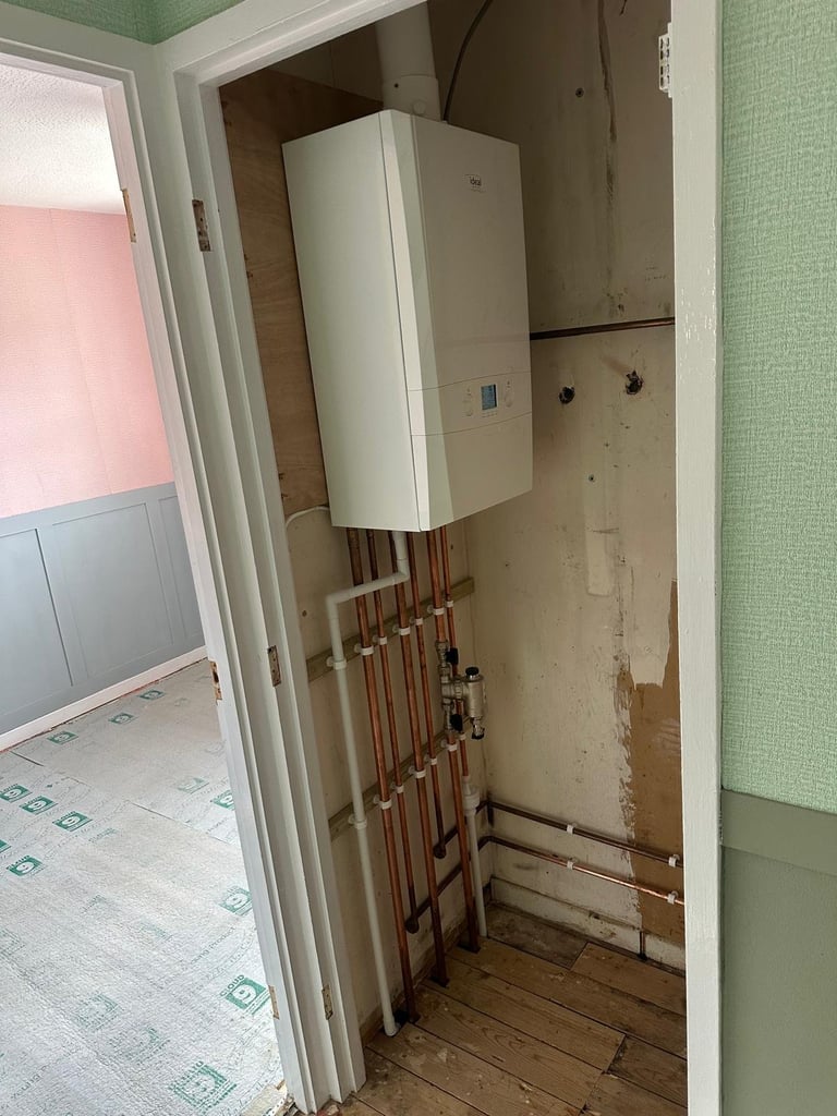 Wall-mounted white tankless water heater with copper pipes in a utility closet during renovation