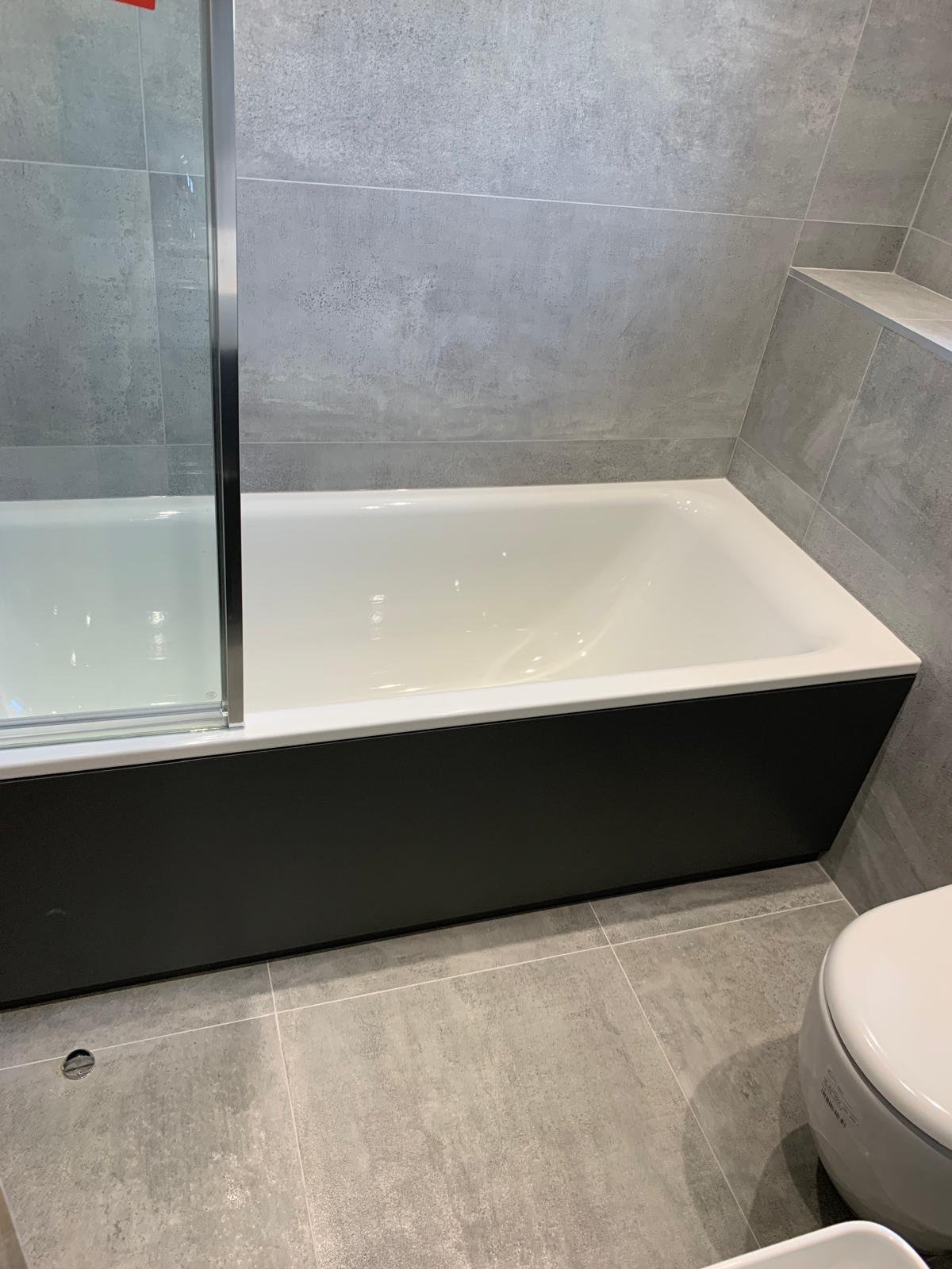 Modern bathroom with black and white bathtub, glass shower partition, gray tile walls and floor, and white toilet