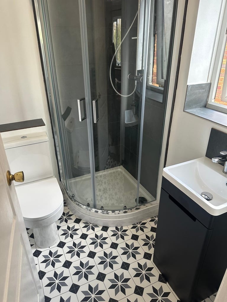 Modern bathroom with black and white geometric floor tiles, curved glass shower enclosure, white toilet, and black vanity with white sink