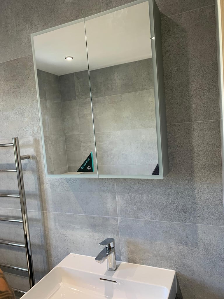 Modern bathroom with white rectangular mirror cabinet above white sink with chrome faucet, gray tiled walls, and heated towel rack