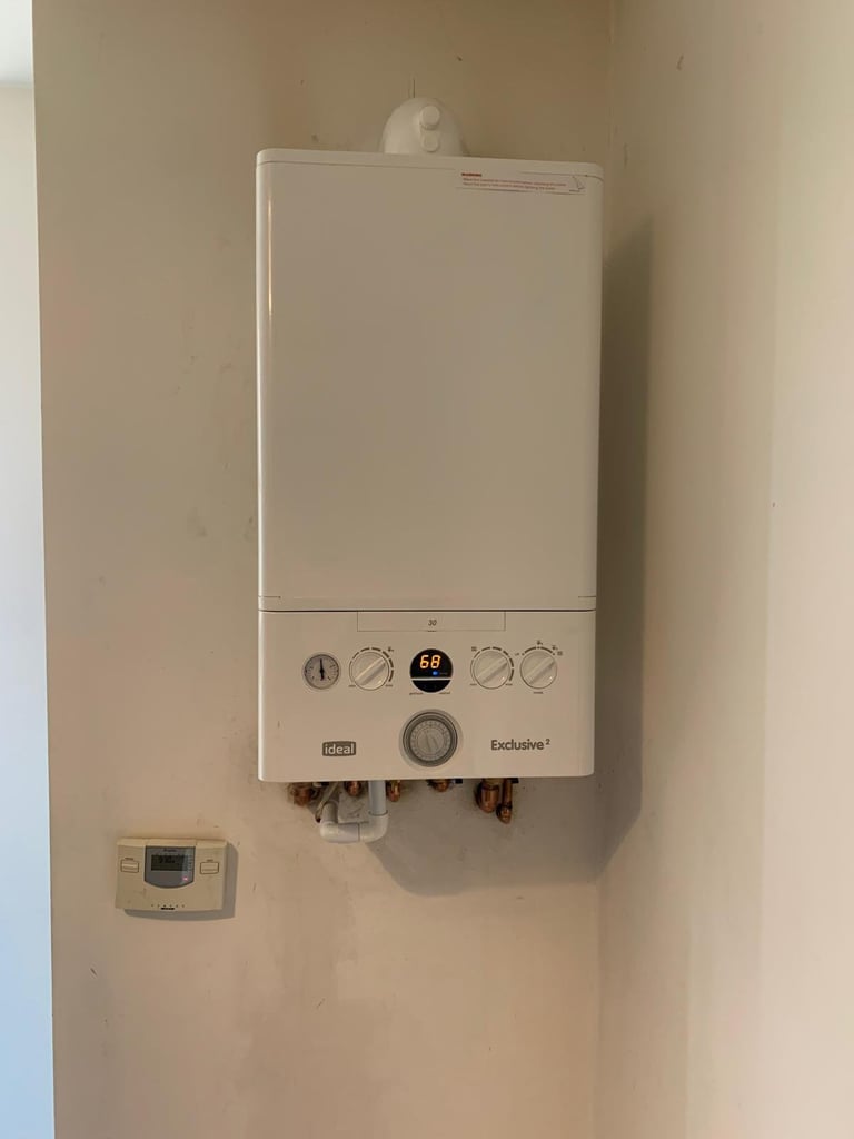 White wall-mounted boiler unit with control dials and a thermostat panel mounted on a beige wall