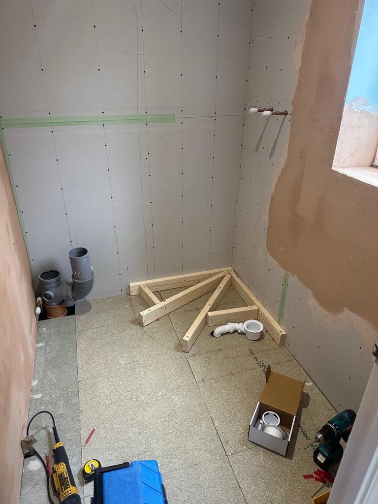 Interior bathroom renovation in progress with drywall, green tape, wooden framing, and construction tools scattered on concrete floor