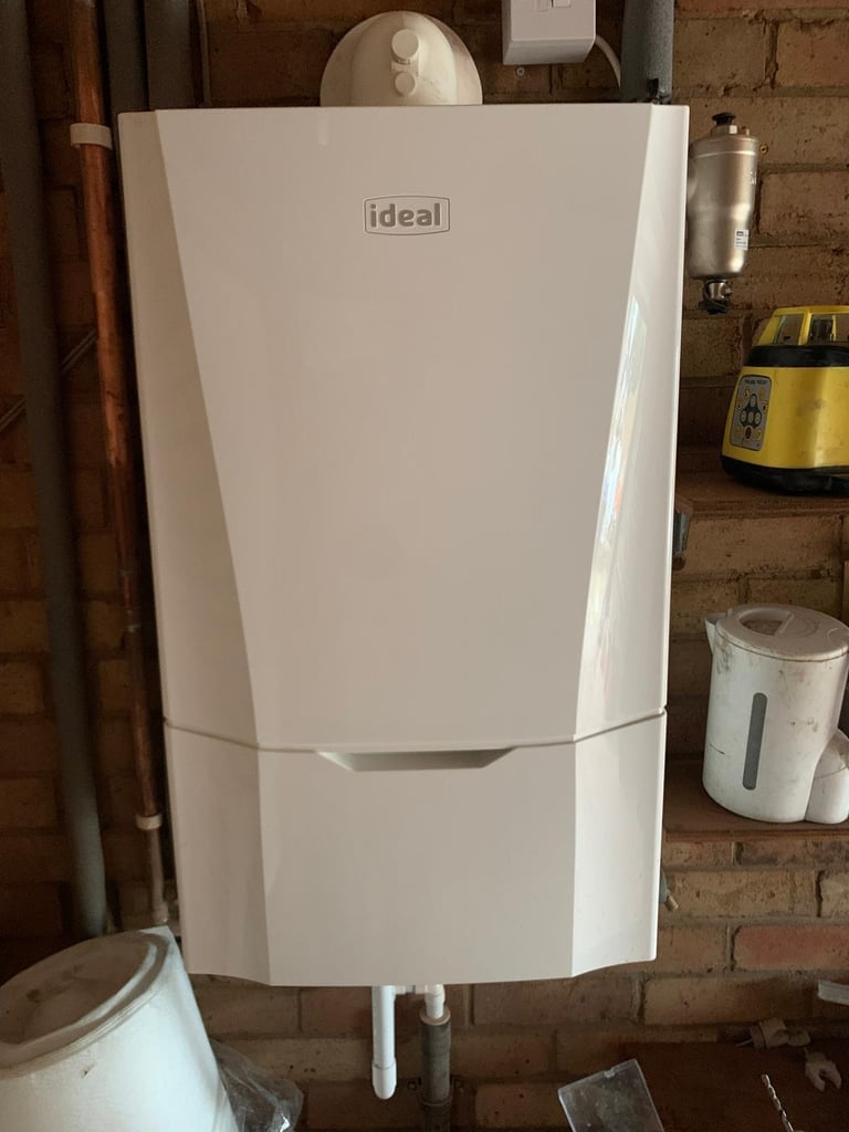 White Ideal brand wall-mounted boiler installed on a brick wall with copper pipes and surrounding storage containers