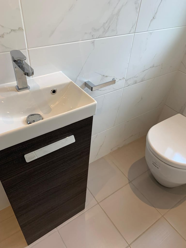 Modern bathroom with white marble-effect wall tiles, compact sink with black vanity cabinet, chrome faucet, and white toilet