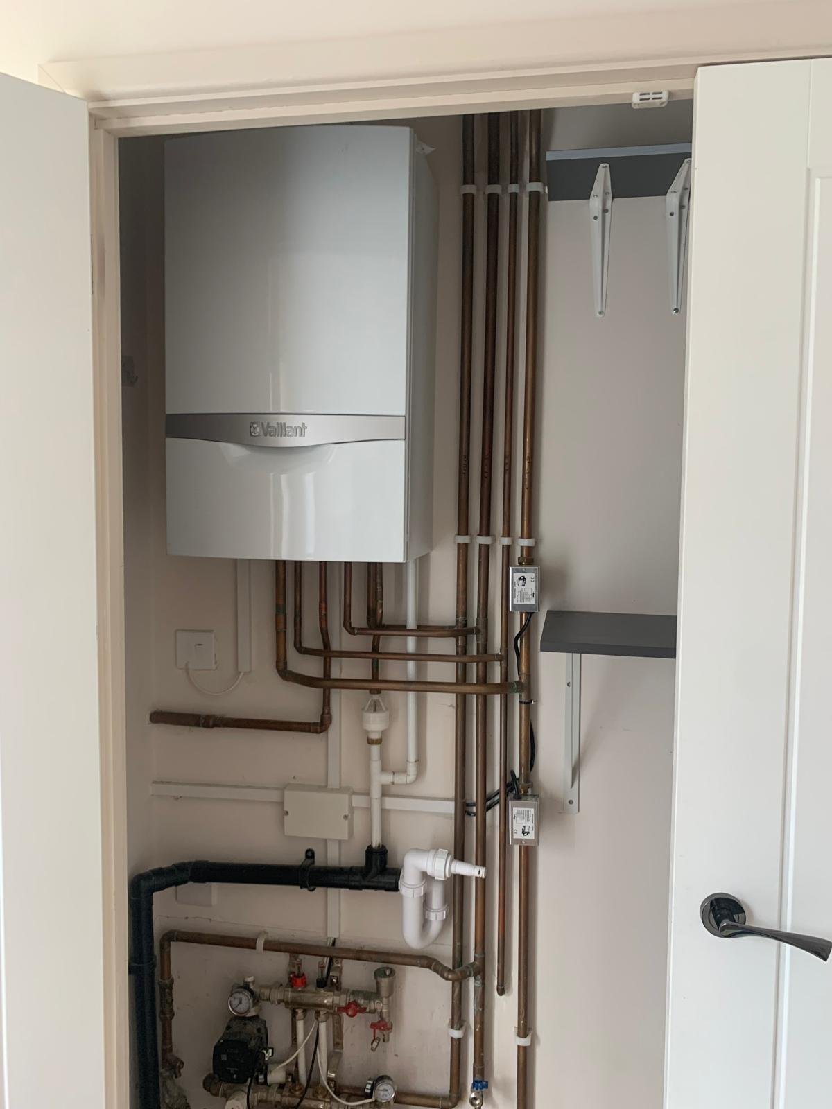 Modern wall-mounted boiler system with heating pipes and control panels installed in a utility closet